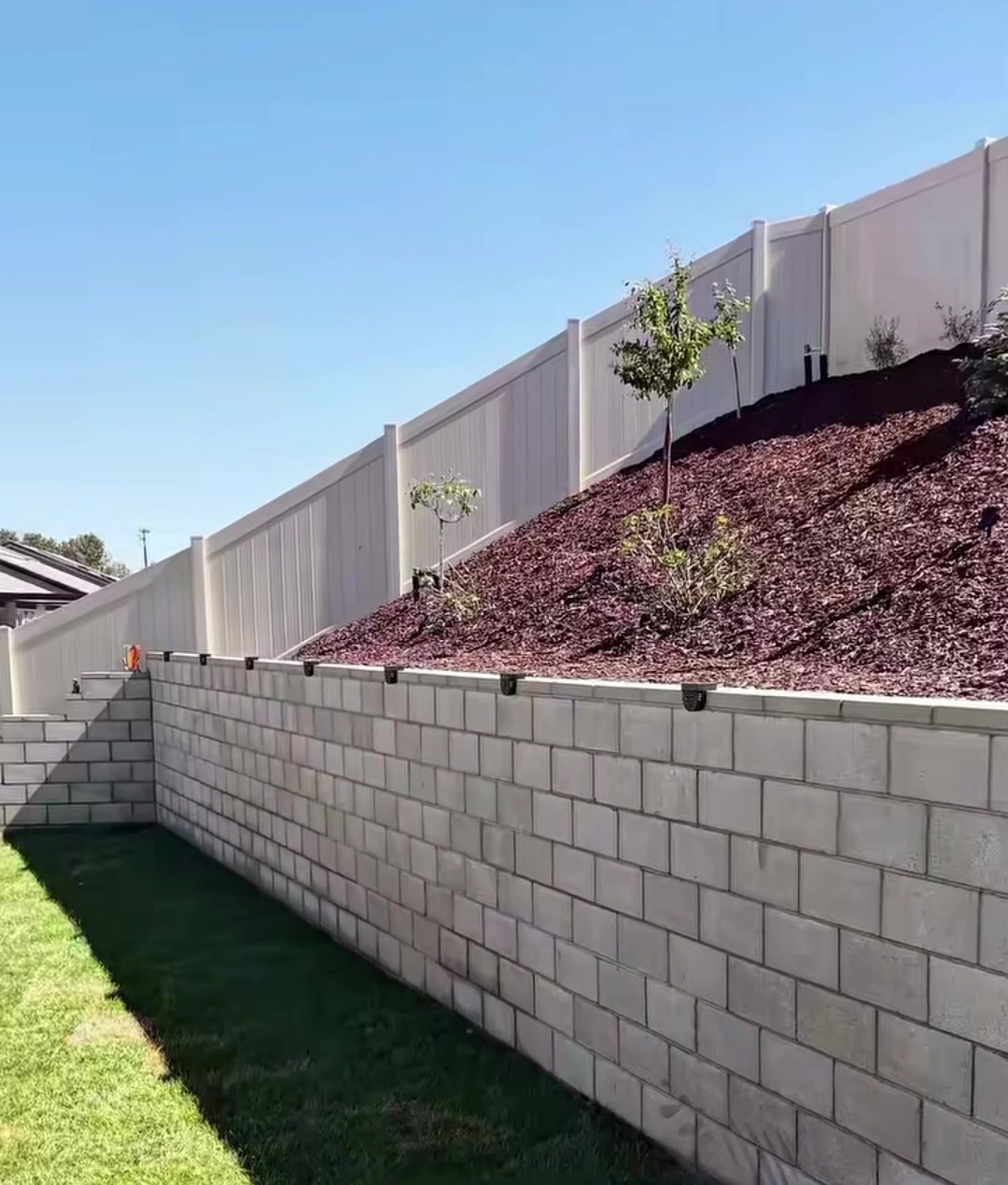 After: a block masonry wall holding back the slope, with fresh sod below and mulch above
